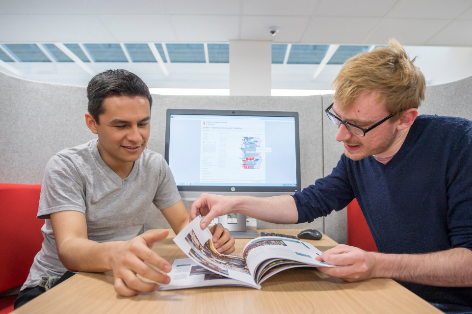 A male staff member helping a male student reading through a book.